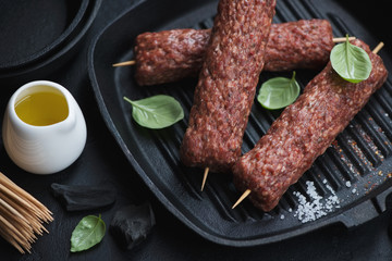 Cast-iron grill pan with uncooked marbled beef kabobs on wooden skewers, close-up, studio shot