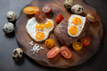 Grilled marbled beefsteak with fried quail eggs and cherry tomatoes on a wooden serving board, studio shot, closeup