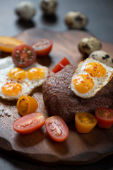 Close-up of bbq marbled beef steak served with cherry tomatoes and fried quail eggs, selective focus