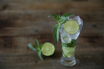 Mojito cocktail in glass with ice, mint and green lime on a wooden rustic background. With copy space for text. Closeup.