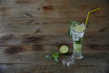  Cocktail Mojito in glass with ice, mint and green lime on a wooden rustic background with copy space for text.