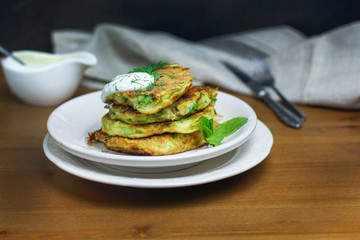 Proper nutrition, vegetarian breakfast gluten free,zucchini courgette pancakes with beans, mint on white plates with sour greek yogurt, black background, towel, fork, knife on wooden surface