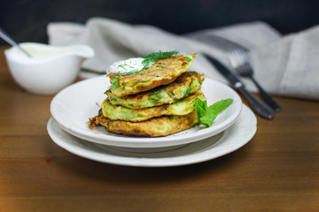 Proper nutrition, vegetarian breakfast gluten free,zucchini courgette pancakes with beans, mint on white plates with sour greek yogurt, black background, towel, fork, knife on wooden surface