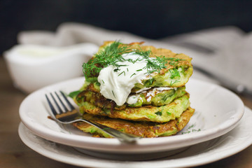 Proper nutrition, vegetarian breakfast gluten free,zucchini courgette pancakes with beans, mint on white plates with sour greek yogurt, black background, towel, fork, knife on wooden surface