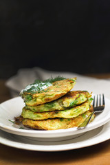 Proper nutrition, vegetarian breakfast gluten free,zucchini courgette pancakes with beans, mint on white plates with sour greek yogurt, black background, towel, fork, knife on wooden surface