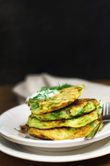 Proper nutrition, vegetarian breakfast gluten free,zucchini courgette pancakes with beans, mint on white plates with sour greek yogurt, black background, towel, fork, knife on wooden surface