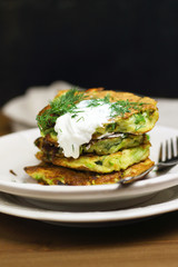 Proper nutrition, vegetarian breakfast gluten free,zucchini courgette pancakes with beans, mint on white plates with sour greek yogurt, black background, towel, fork, knife on wooden surface