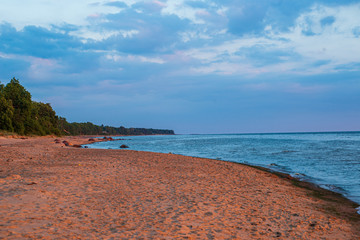Fototapeta premium lonely empty sea beach with white sand, large rocks and old wooden trunks on the shore