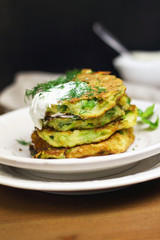 Proper nutrition, vegetarian breakfast gluten free,zucchini courgette pancakes with beans, mint on white plates with sour greek yogurt, black background, towel, fork, knife on wooden surface