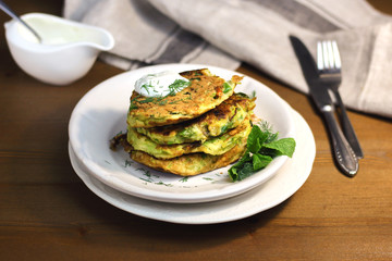 Proper nutrition, vegetarian breakfast gluten free,zucchini courgette pancakes with beans, mint on white plates with sour greek yogurt, black background, towel, fork, knife on wooden surface