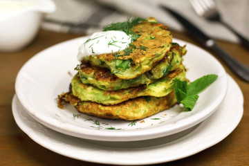 Proper nutrition, vegetarian breakfast gluten free,zucchini courgette pancakes with beans, mint on white plates with sour greek yogurt, black background, towel, fork, knife on wooden surface