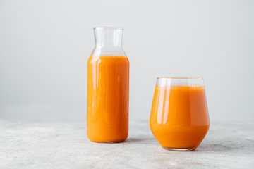 Fresh squeezed carrot juice in bottle and glass on wooden table isolated over white background. Vegetable beverage. Healthy drink.