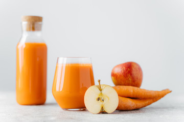Horizontal shot of detox carrot juice in bottle and glass, slice of apple, carrot, isolated over white background. Healthy natural drink. Selective focus