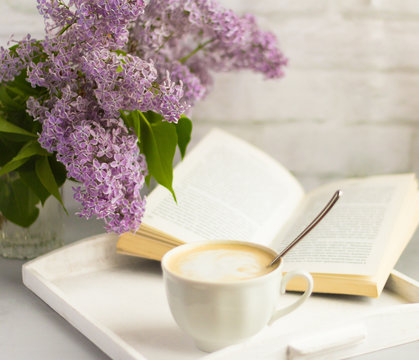 a Cup of hot coffee with milk,a bouquet of lilacs and an open book on the table,rest time