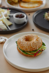Bagels with cream, avocado, salmon, tomatos on wooden board and table beige background. Healthy breakfast food