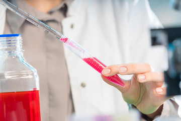 Young woman in scientific lab with pipette and chemicals in test tubes