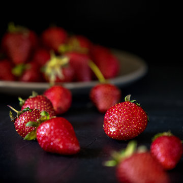 Strawberries, scattered and in a plate on a dark background under the concrete.
