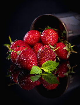 Strawberries, on a dark transparent background, spilled out of a metal black jar.