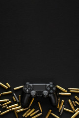 Modern black gamepad on a black background among the spent cartridges. Game concept. Shooter game. © solidmaks
