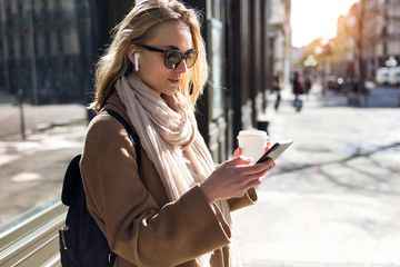Pretty young woman listening to music with wireless earphones and the smartphone in the street.