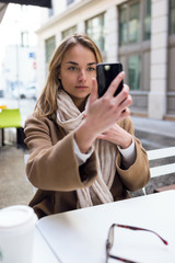 Pretty young woman looking at her mobile phone while sitting on the terrace of a coffee shop.