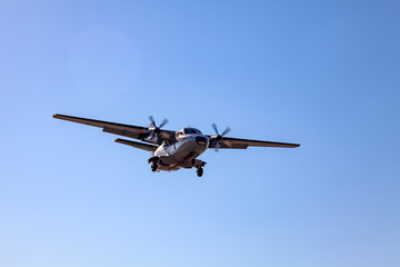 A small aircraft for the transport of passengers and paratroopers lands in a field on a landing strip with grass under a blue sky above the trees on a clear cloudless day. Air patrol.
