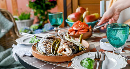 Griddle with shrimps in hand. Dining table with different foods, snacks and flowers. Summer lunch in the open air. Seafood and asparagus. Sun flare on the photo.