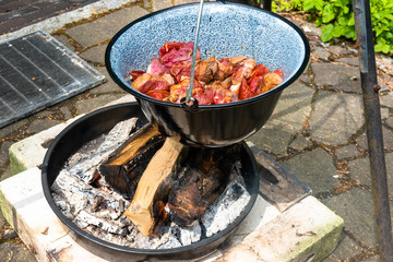 Frying the raw beef in a cauldron over an open wood fire to prepare the Hungarian cauldron goulash, food