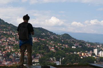Fototapeta na wymiar Bosnia and Herzegovina: a man from behind looking at the breathtaking skyline of Sarajevo, surrounded by the Dinaric Alps and situated along the Miljacka River, from the Zuta Tabija (Yellow Fortress) 
