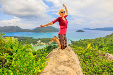 Praslin, Seychelles freedom woman jumping. Joyful happy tourist jumper at lookout of island after hiking inside Reserve of Fond Ferdinand. Scenic top view of Bay of St. Anne. Tropical summer holidays.
