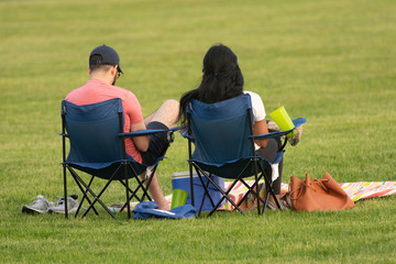 unknown couple sitting in beach chairs is enjoying a sunny day at the park