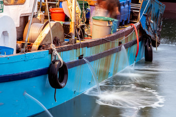Flow of water from fishing boats gunwales during ballast discharge as vessel docked in harbor.