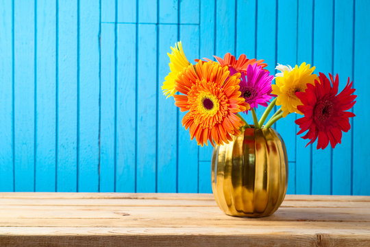 Colorful flower bouquet in golden vase on wooden table.