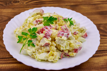 Salad with crab sticks, sweet corn, chinese cabbage, eggs and mayonnaise on wooden table