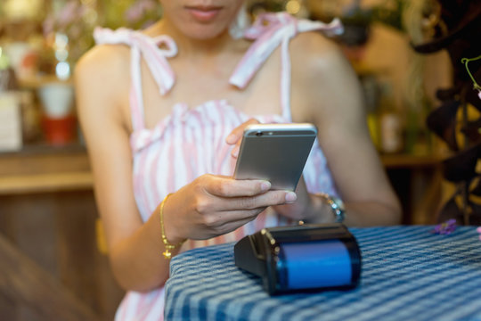 close up customer woman hand using mobile phone for paying bill by payment machine to at table in the cafe , contactless payment concept