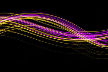 Long exposure, light painting photography.  Vibrant neon pink and gold streaks of colour against a black background