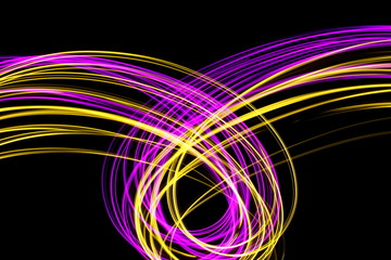 Long exposure, light painting photography.  Vibrant neon streaks and loops of pink and gold colour against a black background