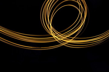 Long exposure, light painting photography.  Vibrant loops of metallic gold colour against a black background