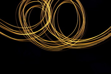 Long exposure, light painting photography.  Vibrant loops of metallic gold colour against a black background