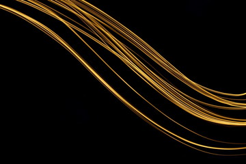 Long exposure, light painting photography.  Vibrant streaks of metallic gold colour against a black...