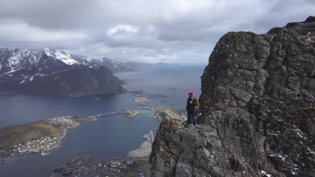 Aerial footage of male hiker on mountain top overlooking beautiful Lofoten Islands scenery in scenic , Archipelago Norway,