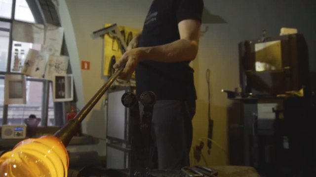 Glassblower in his workshop taking out rod with liquid glass and turning it. Close-up.