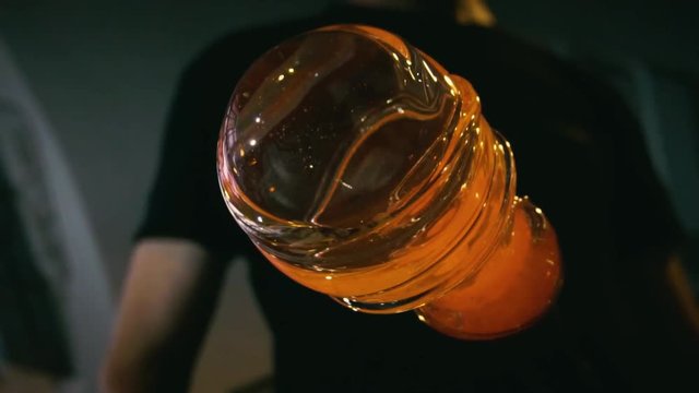 Glassblower in his workshop taking out rod with liquid glass and turning it. Close-up.