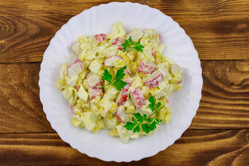 Salad with crab sticks, sweet corn, chinese cabbage, eggs and mayonnaise on wooden table