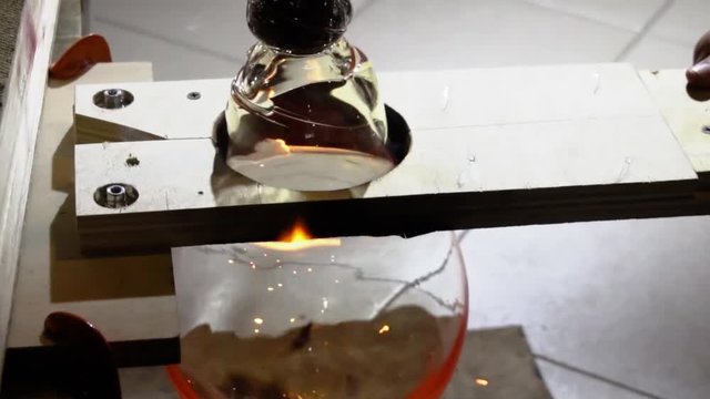Glassblower in his workshop taking out rod with liquid glass and turning it. Close-up. Slow motion.