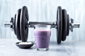 Glass of Protein Shake with milk and blueberries, Beta-alanine capsules and a dumbbell in background. Sports bodybuilding nutrition. Stone / Wooden background. Copy space.  