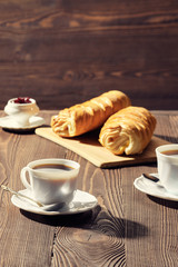 Rolled buns and coffee on wooden table in morning sunlight