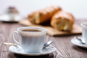 Rolled buns and coffee on wooden table in morning sunlight. Photo with shallow depth of field.