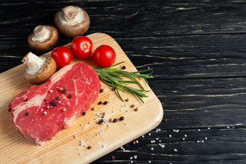 One pieces of juicy raw beef on a cutting board on a black wooden table background.
