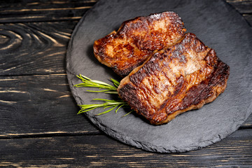 juicy piece of fried meat lies on a stone plate against a black wooden table
